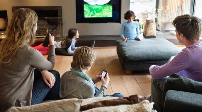Group of people lounging in a living room watching TV, scrolling on smartphones. 