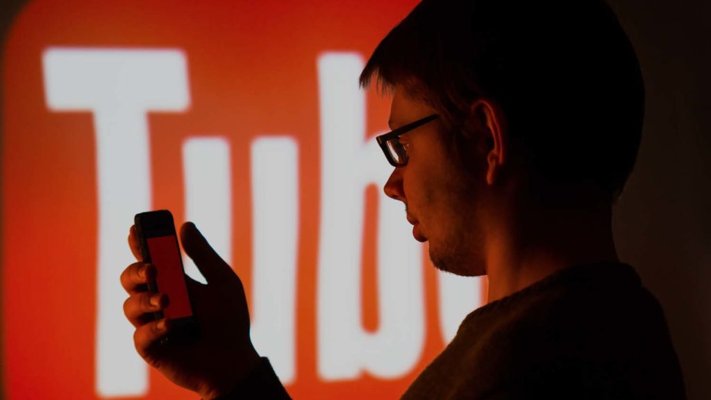 Man looking at smartphone screen with YouTube logo partially in view in the background. 