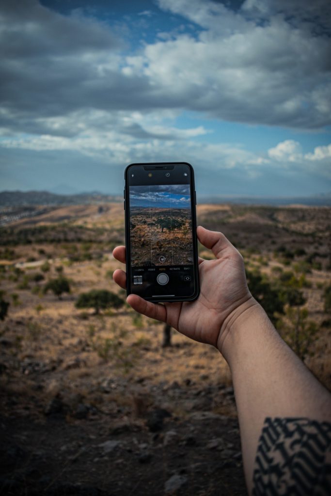 A cell phone taking a picture of a beautiful desert landscape with clouds.