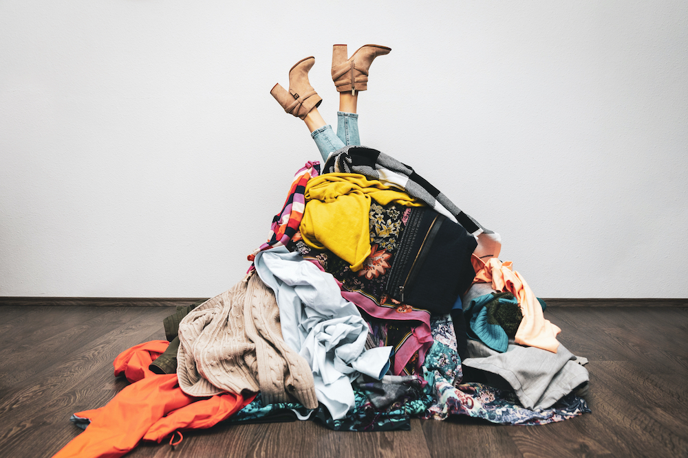A pair of legs sticking out under clothing that's messily gathered in a large pile. 
