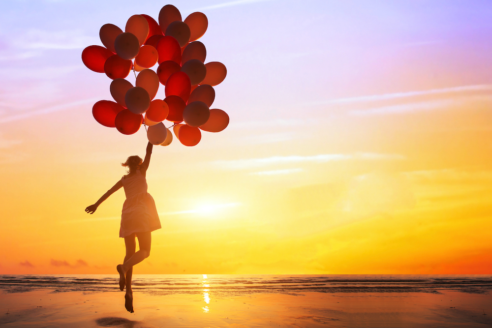 Woman with a bunch of balloons skipping on the beach during sunset. 