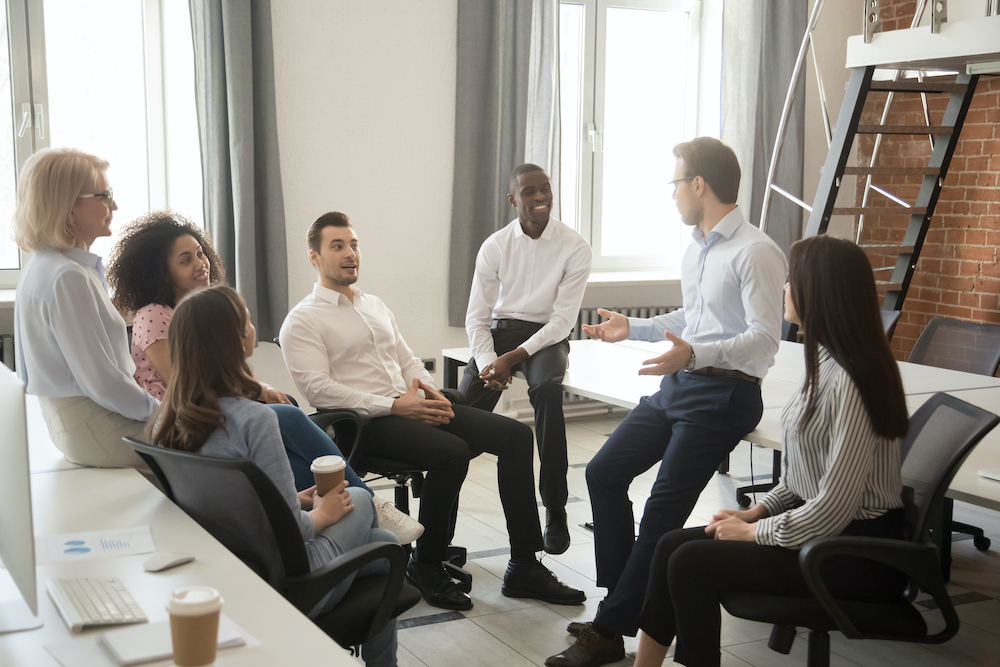 Multiethnic workgroup talk during a casual office meeting, discuss business ideas sharing thoughts, smiling diverse colleagues or employees speak negotiating at an informal briefing at workplace
